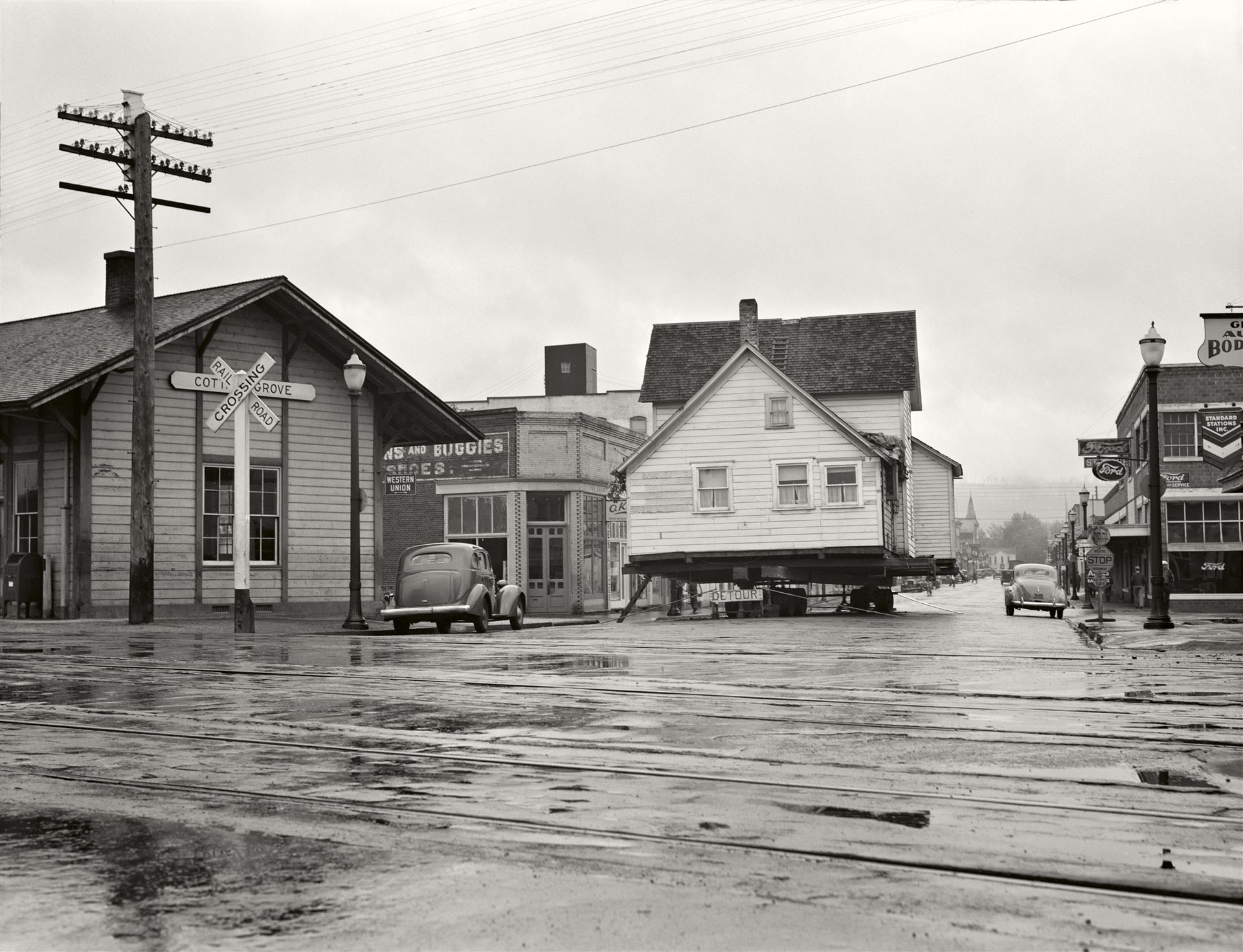 Dorothea Lange, <i>Una casa viene spostata nella strada principale della città (2473 abitanti). Depositata domenica all'incrocio della U.S. 99. Pomeriggio tranquillo e piovoso Cottage Grove</i>, Lane County, Oregon, 1939<br>© Dorothea Lange<br><br>